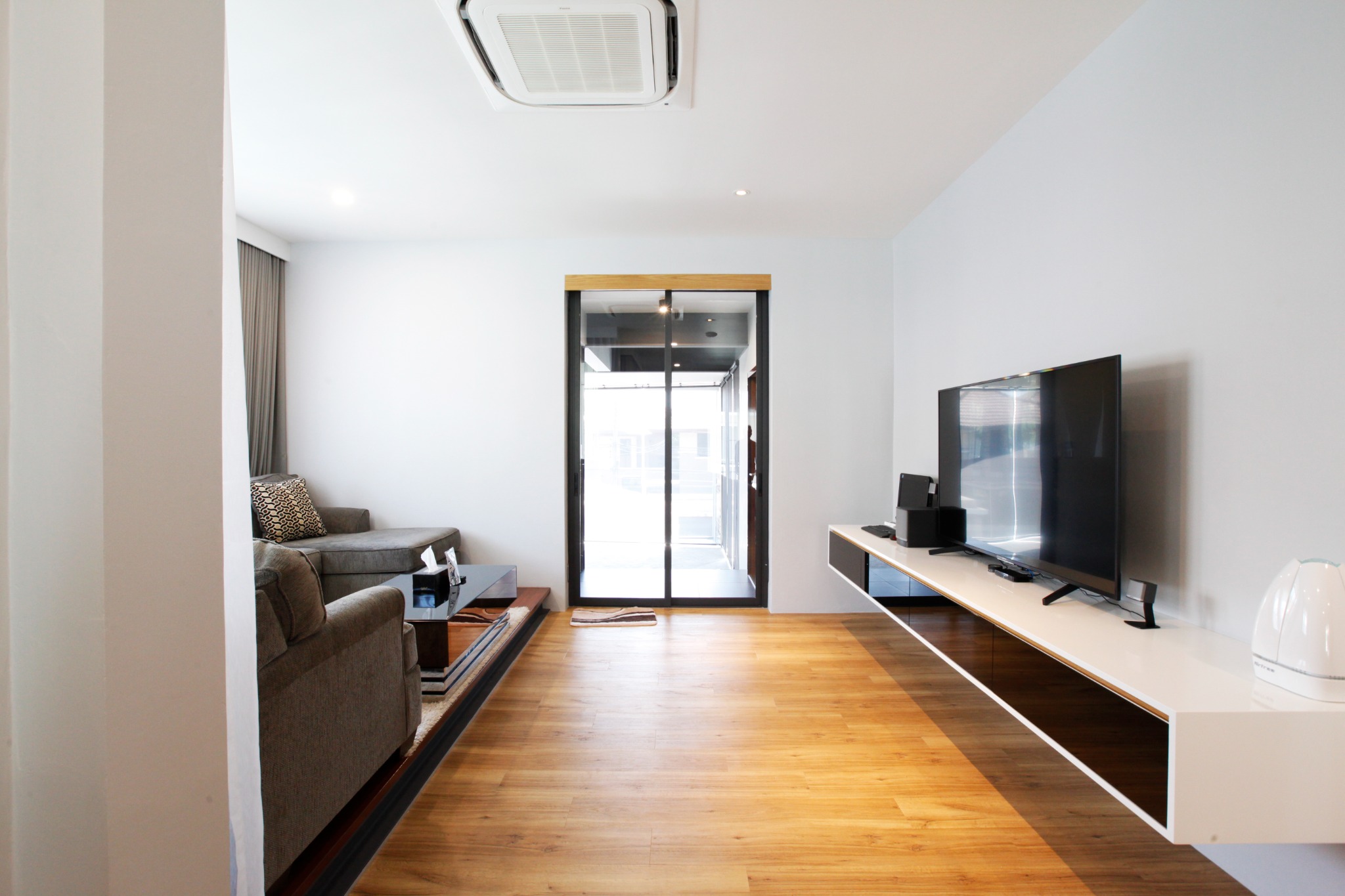Living room view toward the entrance with timber flooring and a built-in television console