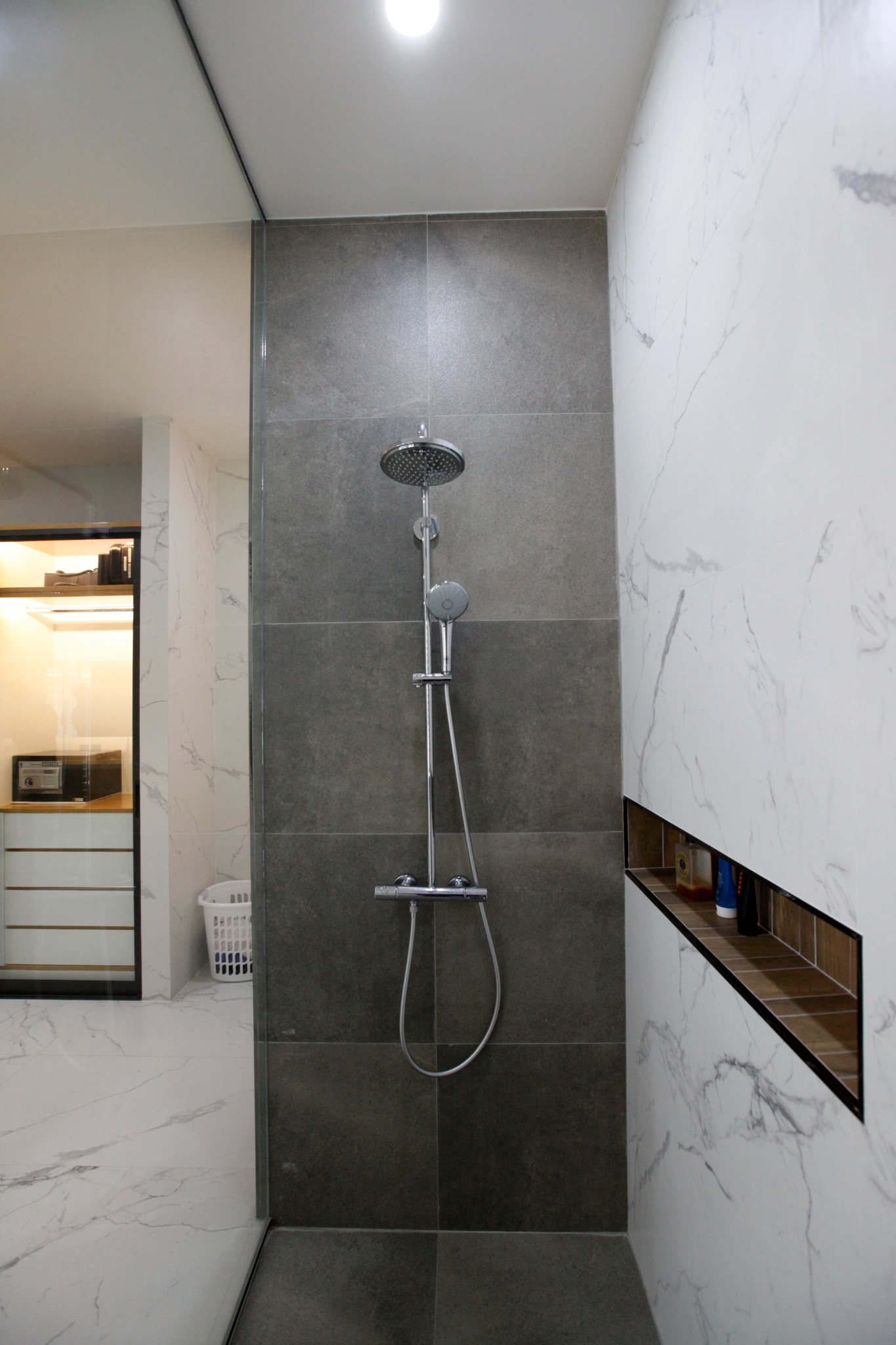 Shower area with grey tiles, marble walls and a recessed shelf