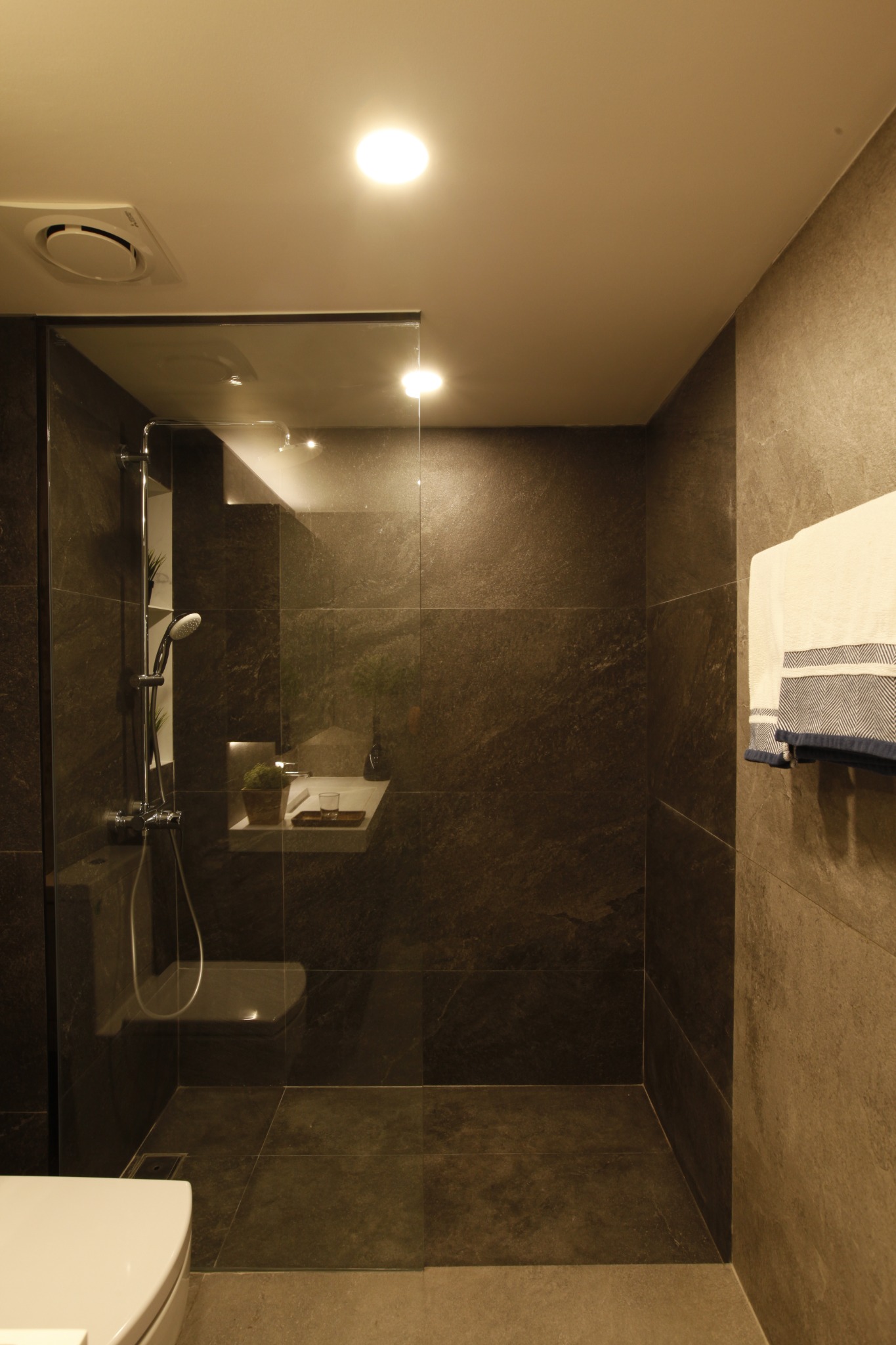 Dark tiled shower area with recessed shelf and glass partition